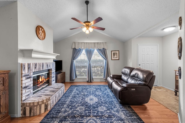 living room with lofted ceiling, ceiling fan, wood-type flooring, a textured ceiling, and a brick fireplace