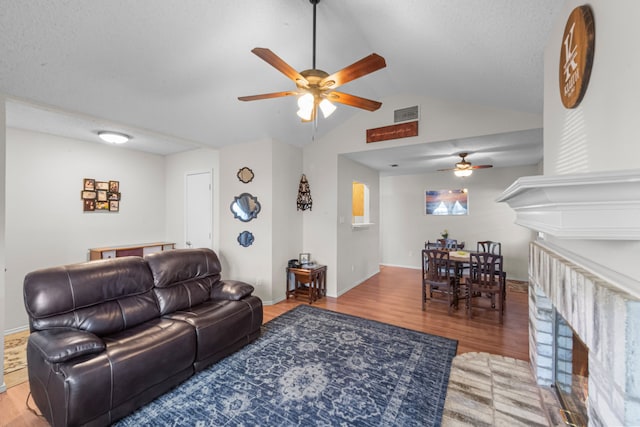 living room with a textured ceiling, light hardwood / wood-style flooring, ceiling fan, and vaulted ceiling