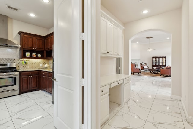 kitchen featuring white cabinetry, wall chimney exhaust hood, stainless steel gas range, and backsplash