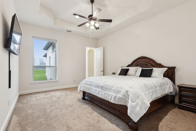 bedroom with ceiling fan, light colored carpet, and a raised ceiling