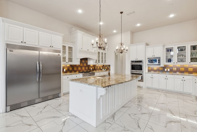 kitchen with white cabinetry, an island with sink, pendant lighting, and built in appliances