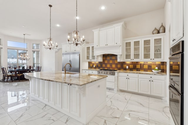 kitchen with white cabinetry, decorative light fixtures, stainless steel appliances, and an island with sink