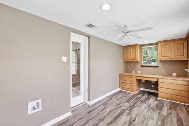 unfurnished office featuring built in desk, ceiling fan, and light hardwood / wood-style flooring