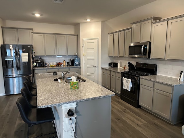 kitchen featuring sink, light stone countertops, an island with sink, and appliances with stainless steel finishes