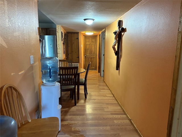 hallway with a textured ceiling and light hardwood / wood-style flooring