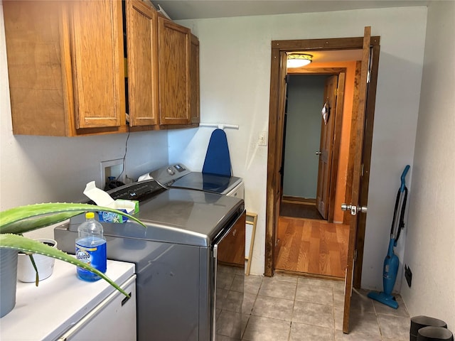 clothes washing area featuring cabinets, washer and clothes dryer, and light tile patterned floors