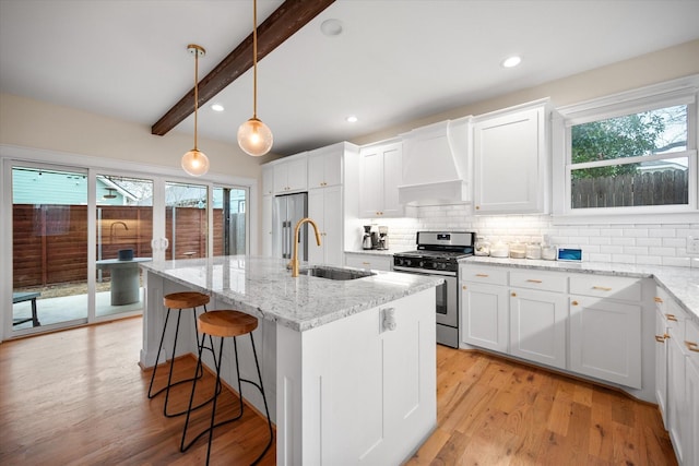 kitchen featuring premium range hood, decorative light fixtures, white cabinetry, sink, and stainless steel appliances