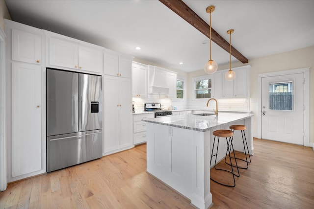 kitchen with white cabinetry, sink, light stone counters, stainless steel appliances, and custom range hood