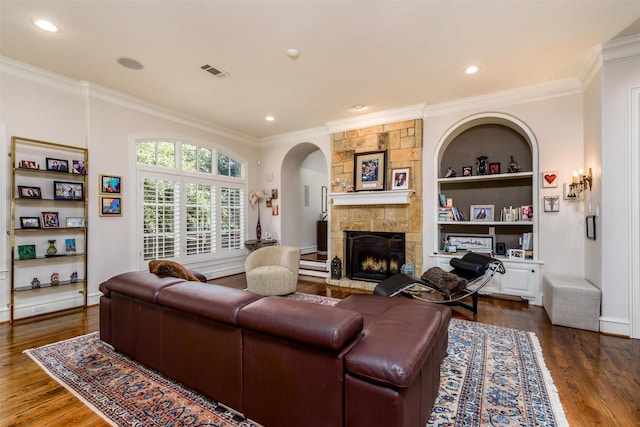 living room featuring dark hardwood / wood-style floors, a fireplace, built in shelves, and crown molding