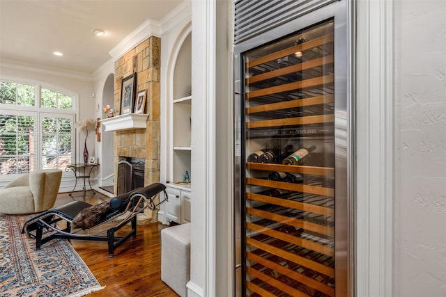 wine area with dark wood-type flooring, wine cooler, a fireplace, ornamental molding, and built in shelves