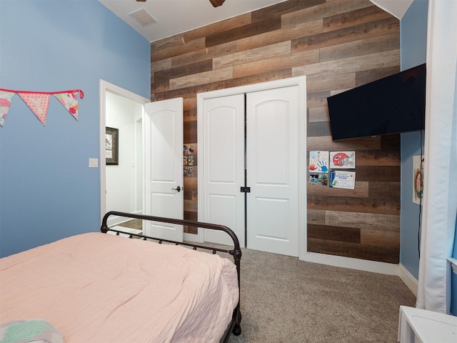 carpeted bedroom featuring ceiling fan, wooden walls, and a closet