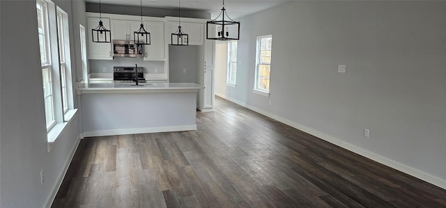 kitchen featuring appliances with stainless steel finishes, dark hardwood / wood-style floors, white cabinetry, sink, and hanging light fixtures