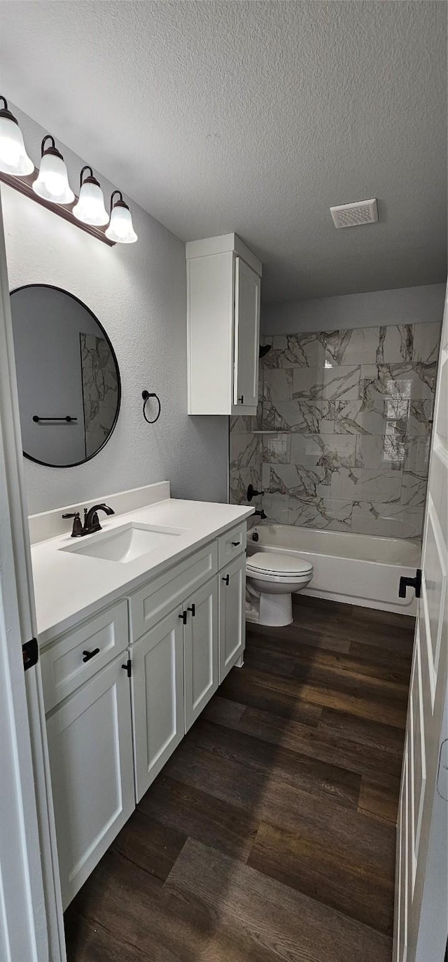 full bathroom with wood-type flooring, vanity, a textured ceiling, and tiled shower / bath