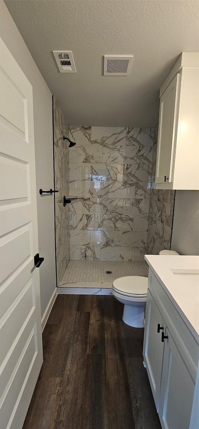 bathroom featuring wood-type flooring, toilet, vanity, and a tile shower