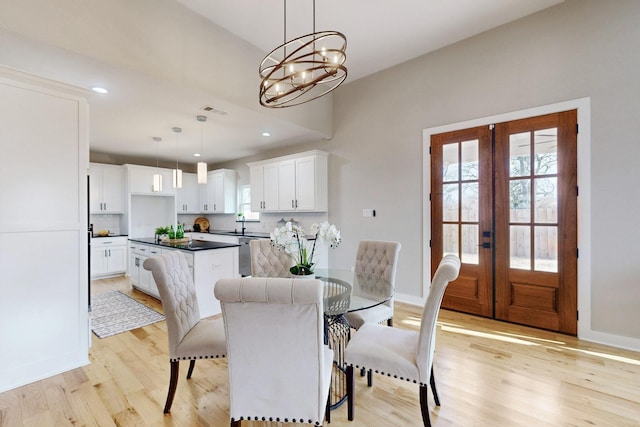 dining area with an inviting chandelier, french doors, light wood finished floors, and baseboards