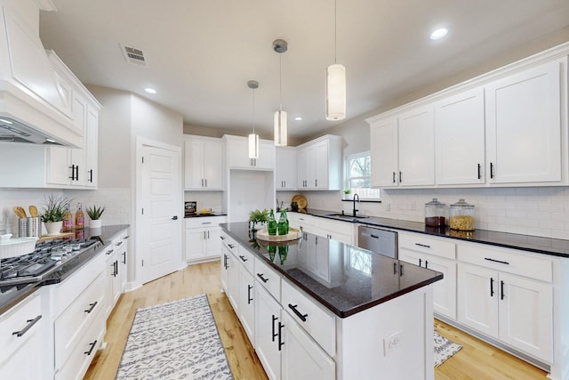 kitchen with a center island, custom exhaust hood, stainless steel appliances, light wood-style floors, and a sink