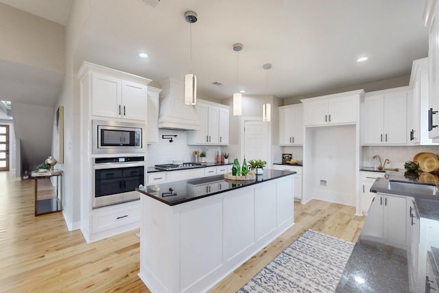 kitchen featuring appliances with stainless steel finishes, dark countertops, premium range hood, and light wood finished floors