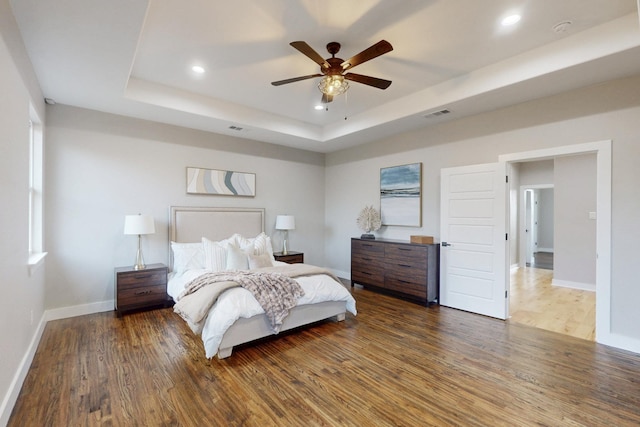 bedroom featuring a tray ceiling, visible vents, baseboards, recessed lighting, and wood finished floors