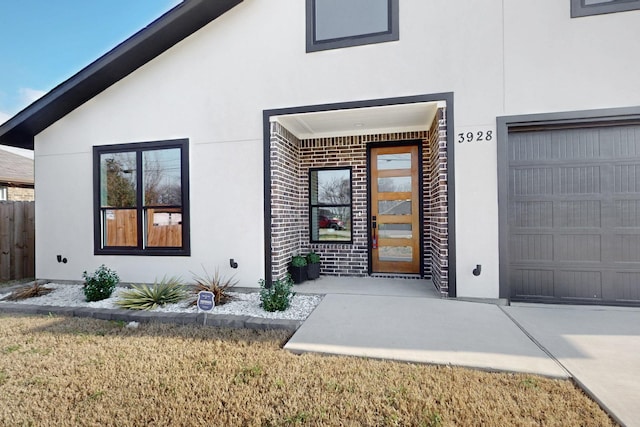 doorway to property featuring a garage, brick siding, fence, and stucco siding