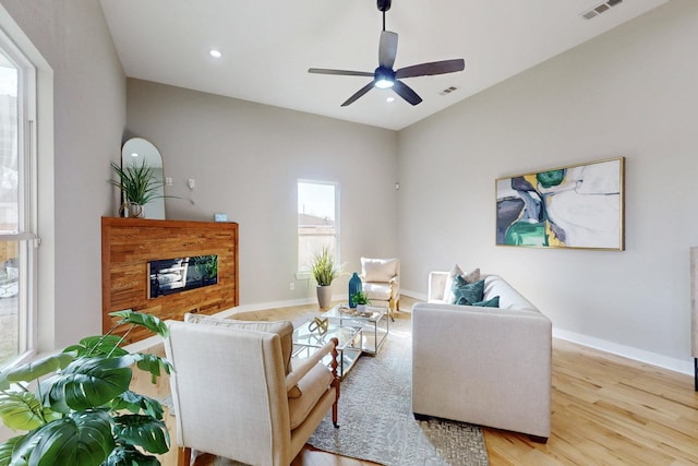 living room featuring light wood-style flooring, visible vents, baseboards, and a glass covered fireplace