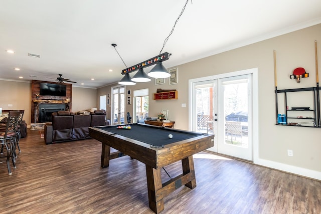 game room featuring french doors, pool table, ornamental molding, dark wood-type flooring, and a large fireplace