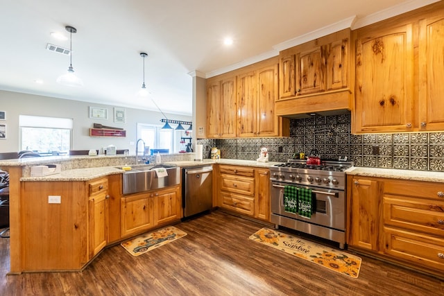 kitchen featuring a peninsula, a sink, appliances with stainless steel finishes, brown cabinetry, and decorative light fixtures