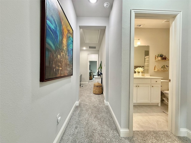 hall featuring baseboards, visible vents, light carpet, and attic access