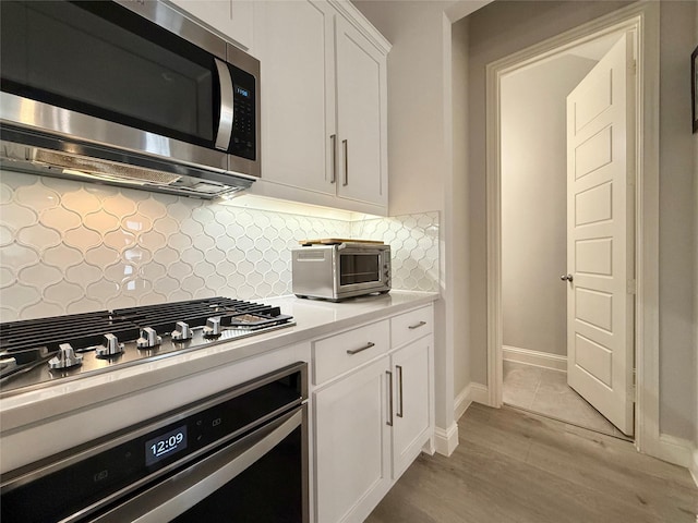 kitchen with tasteful backsplash, a toaster, appliances with stainless steel finishes, light countertops, and white cabinetry