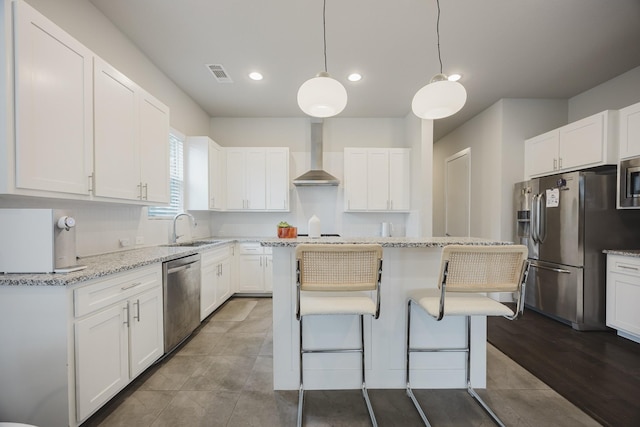 kitchen featuring white cabinetry, hanging light fixtures, appliances with stainless steel finishes, a center island, and wall chimney exhaust hood