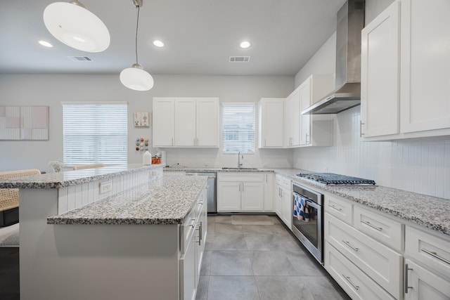 kitchen with decorative light fixtures, visible vents, appliances with stainless steel finishes, white cabinetry, and wall chimney exhaust hood