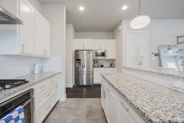 kitchen with under cabinet range hood, stainless steel appliances, white cabinetry, light stone countertops, and decorative light fixtures