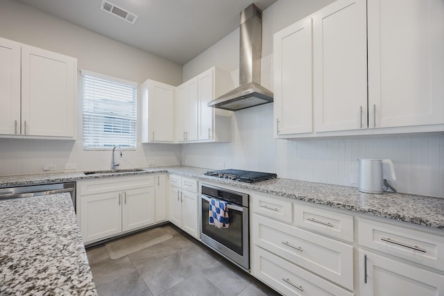 kitchen with visible vents, stainless steel appliances, wall chimney range hood, white cabinetry, and a sink