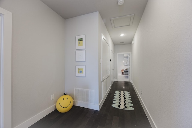 hall with attic access, dark wood-style flooring, visible vents, and baseboards