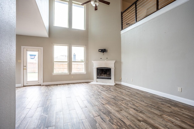 unfurnished living room with hardwood / wood-style floors, ceiling fan, and a high ceiling