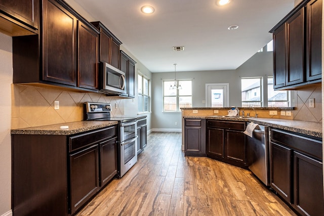 kitchen with appliances with stainless steel finishes, decorative light fixtures, backsplash, dark brown cabinetry, and light hardwood / wood-style floors