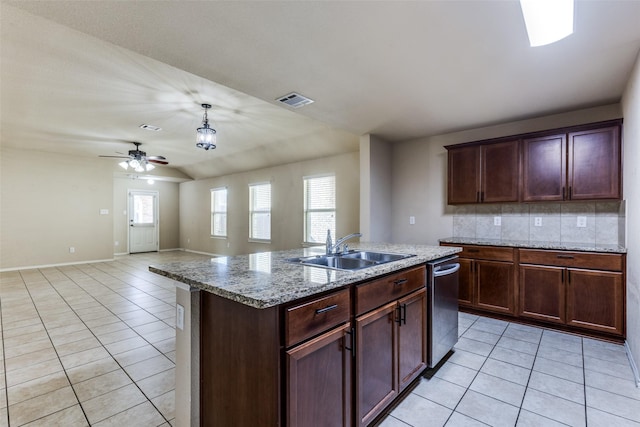 kitchen featuring tasteful backsplash, sink, light tile patterned floors, light stone counters, and a center island with sink