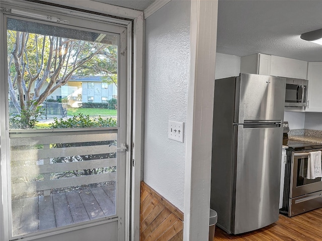 kitchen featuring white cabinetry, appliances with stainless steel finishes, wood-type flooring, and a textured ceiling