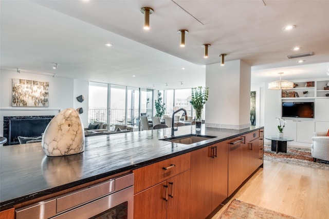 kitchen featuring sink, built in features, a tile fireplace, pendant lighting, and light hardwood / wood-style floors