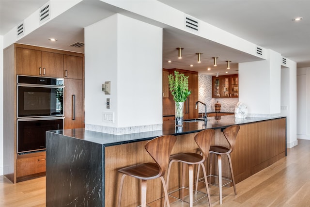 kitchen with sink, tasteful backsplash, light wood-type flooring, kitchen peninsula, and double oven