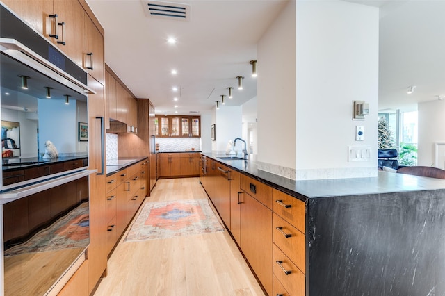 kitchen featuring sink, backsplash, wall oven, kitchen peninsula, and light wood-type flooring