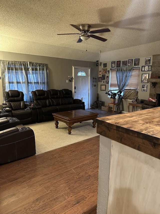 living room featuring a fireplace, ceiling fan, a textured ceiling, and wood finished floors