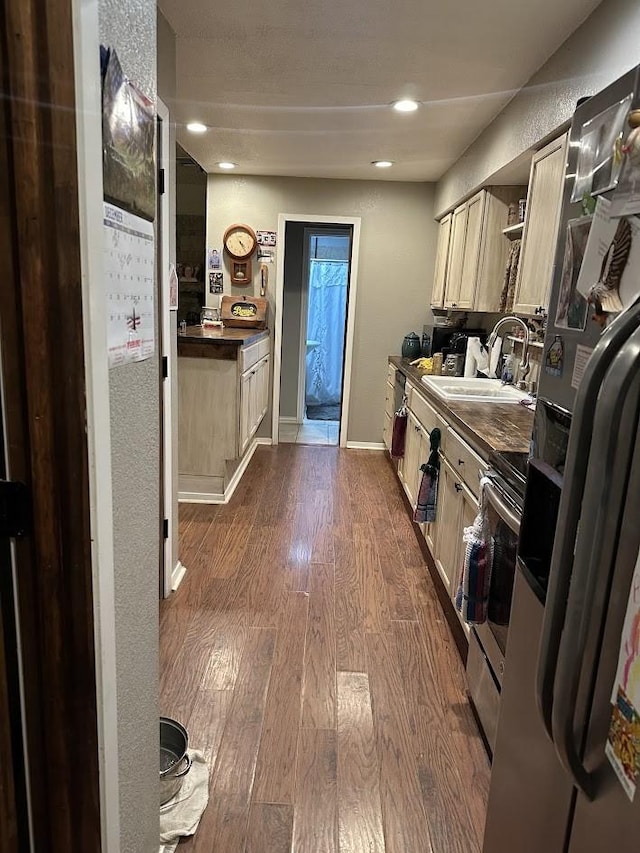 kitchen featuring dark countertops, dark wood-type flooring, stainless steel range with electric cooktop, light brown cabinetry, and a sink