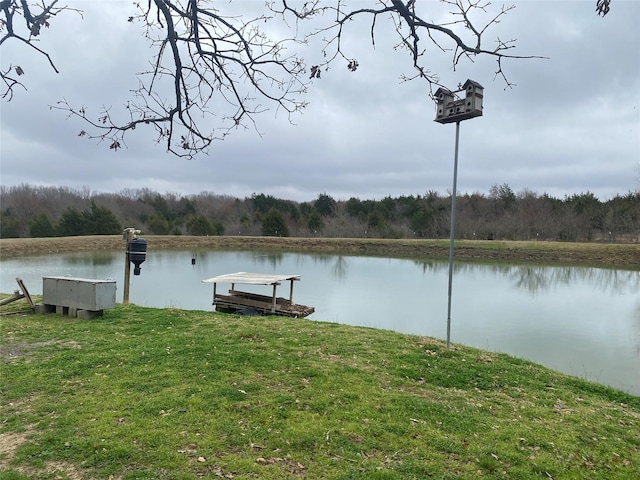 view of dock with a water view, a lawn, and a forest view