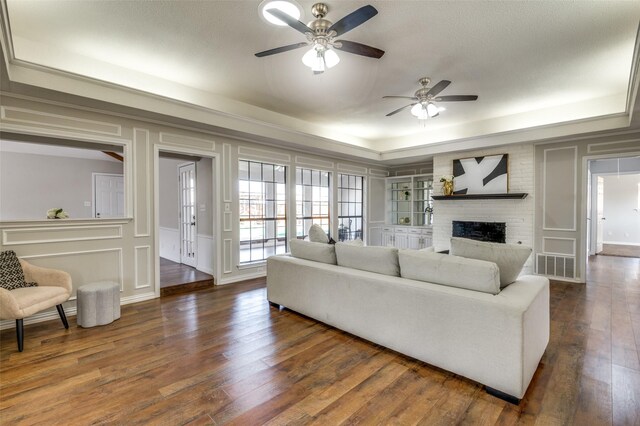 2261 Woodcreek, Carrollton, TX 75006 - living room featuring a brick fireplace, dark wood-type flooring, ceiling fan, and a tray ceiling