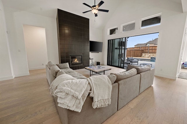 living room with ceiling fan, high vaulted ceiling, a tiled fireplace, and light hardwood / wood-style floors