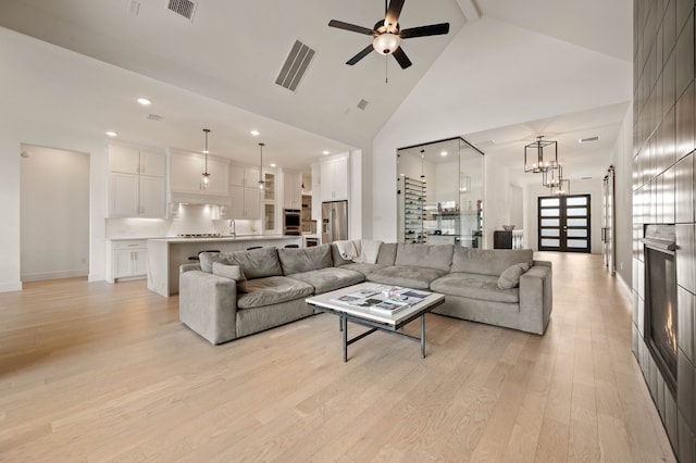 living room with a fireplace, high vaulted ceiling, sink, ceiling fan, and light hardwood / wood-style flooring