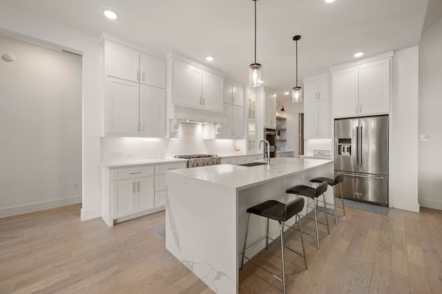 kitchen featuring high quality fridge, a breakfast bar area, white cabinets, backsplash, and a center island with sink