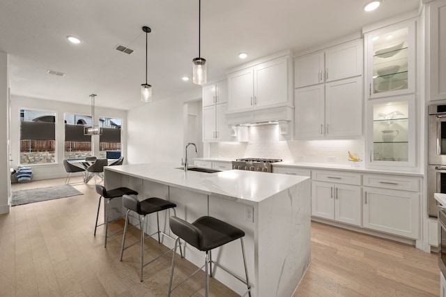 kitchen with sink, white cabinetry, a kitchen breakfast bar, pendant lighting, and a kitchen island with sink