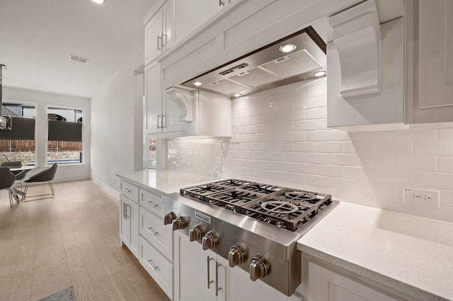 kitchen featuring wall chimney exhaust hood, stainless steel gas cooktop, light wood-type flooring, decorative backsplash, and white cabinets