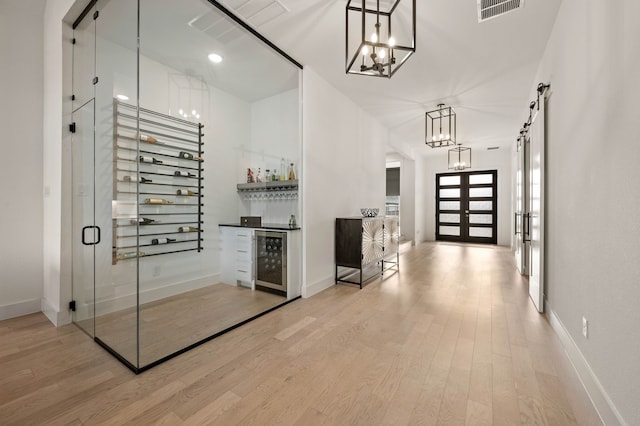 wine room featuring light hardwood / wood-style floors, beverage cooler, a barn door, french doors, and indoor bar